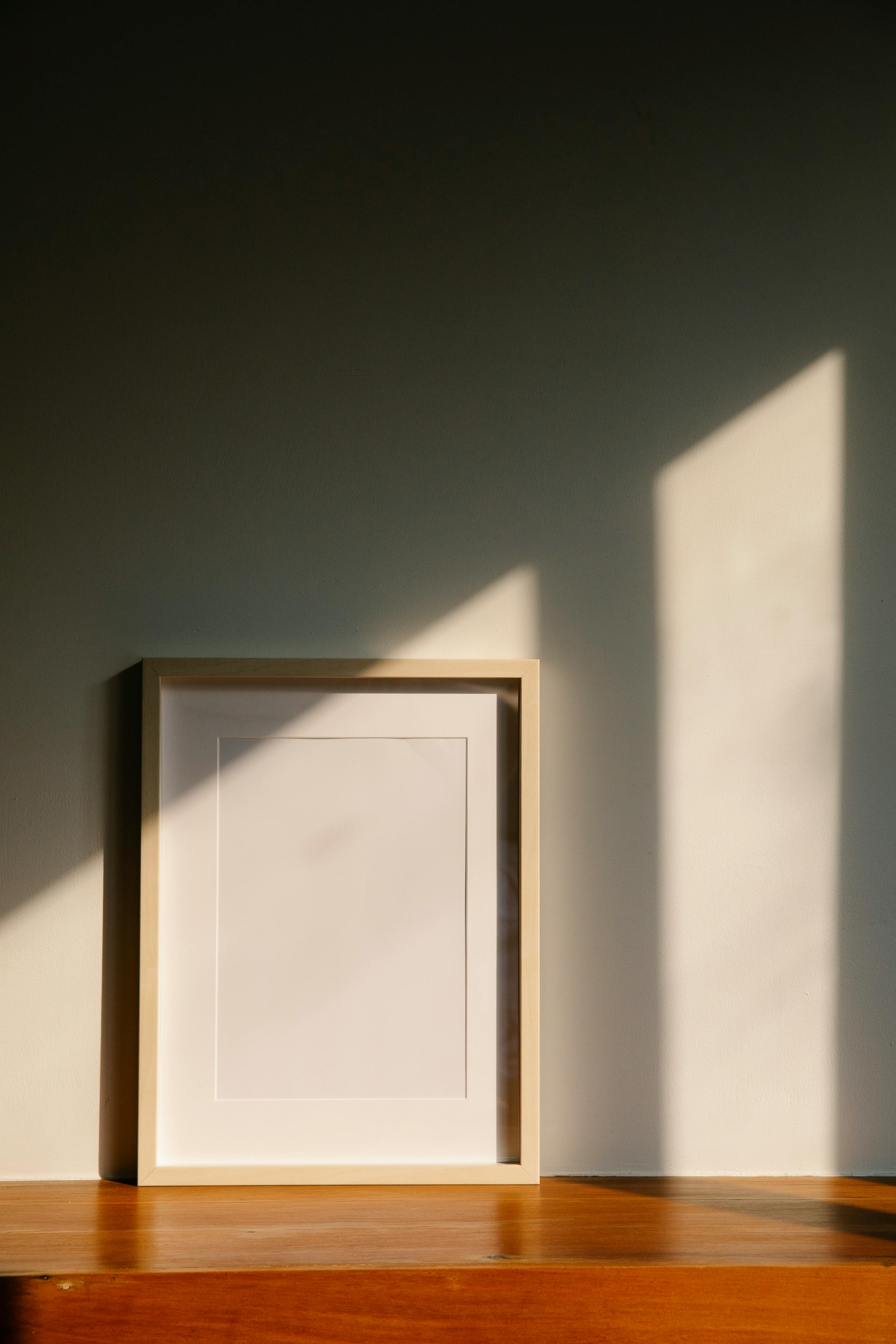 Wooden picture frame on a wooden surface with light casting shadows on a dark wall.